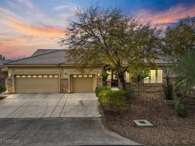 view of front of property featuring a tile roof, stucco siding, a garage, stone siding, and driveway