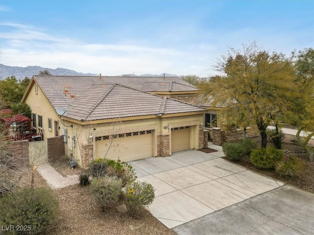 view of front of property featuring fence, concrete driveway, a tile roof, a garage, and stone siding