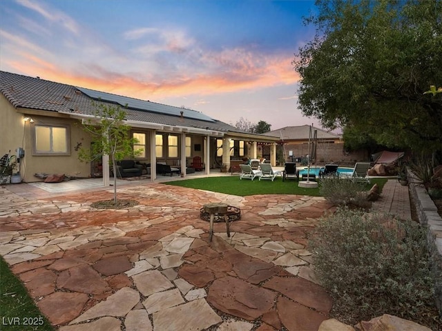 back of house at dusk with roof mounted solar panels, an outdoor hangout area, an outdoor pool, and a patio