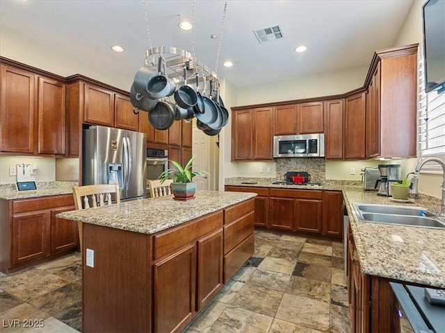 kitchen featuring visible vents, a sink, a center island, appliances with stainless steel finishes, and light stone countertops