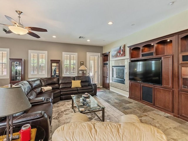 living area featuring visible vents, a glass covered fireplace, recessed lighting, baseboards, and ceiling fan