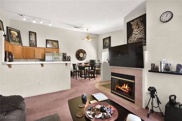 living room featuring a ceiling fan, rail lighting, a fireplace, and light carpet