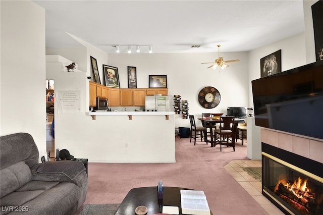 living room featuring visible vents, light carpet, ceiling fan, and a tiled fireplace