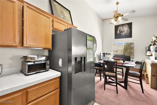 kitchen featuring tile counters, a toaster, ceiling fan, and stainless steel fridge with ice dispenser