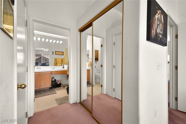 hall featuring light tile patterned floors, light colored carpet, and a sink