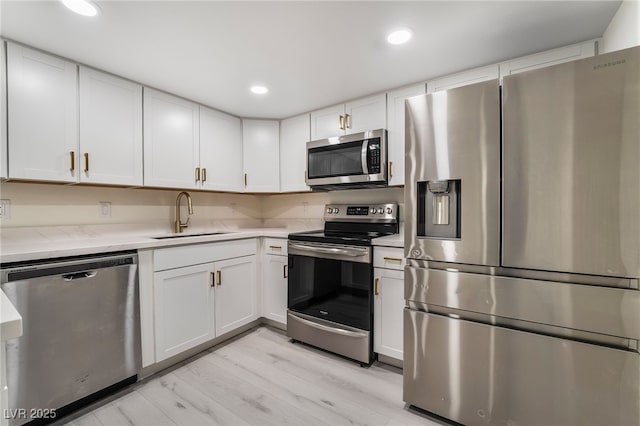 kitchen with a sink, recessed lighting, stainless steel appliances, white cabinets, and light countertops