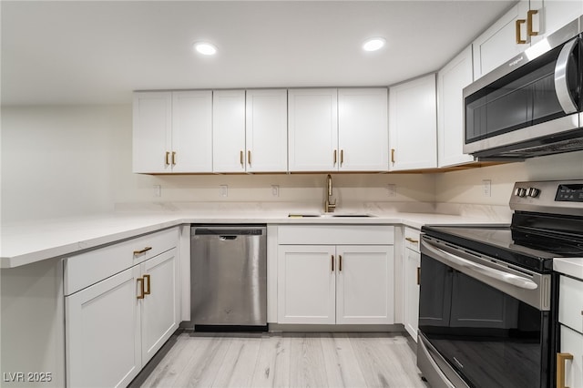 kitchen with light wood finished floors, recessed lighting, a sink, stainless steel appliances, and white cabinetry