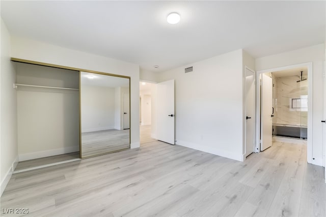 unfurnished bedroom featuring light wood finished floors, visible vents, baseboards, ensuite bathroom, and a closet