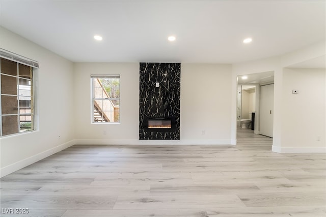 unfurnished living room with a high end fireplace, recessed lighting, light wood-type flooring, and baseboards