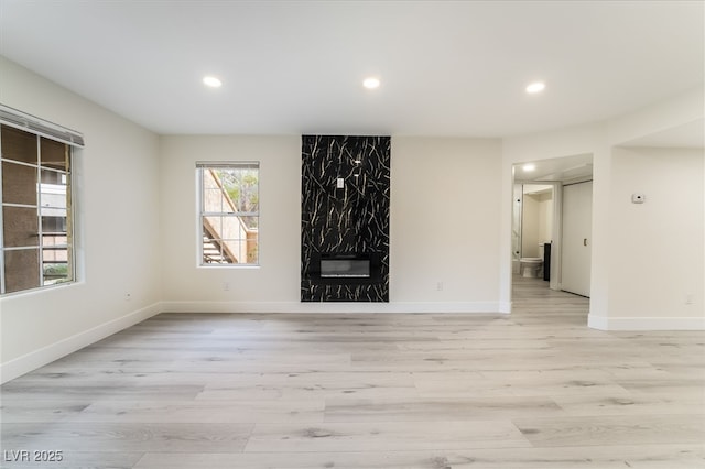 unfurnished living room with recessed lighting, baseboards, a fireplace, and light wood finished floors