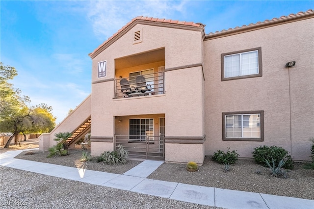 view of front of home featuring stucco siding, a balcony, stairs, and a tiled roof