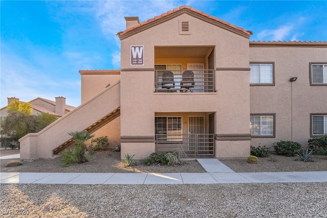 view of front of home with stucco siding, a balcony, a tile roof, and stairway