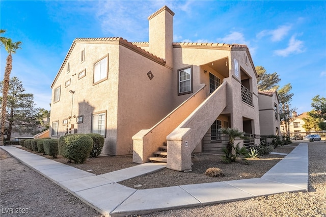 exterior space with stucco siding, a balcony, a chimney, and a tile roof