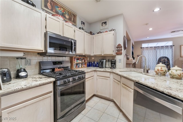 kitchen with light tile patterned floors, light stone countertops, a sink, appliances with stainless steel finishes, and tasteful backsplash