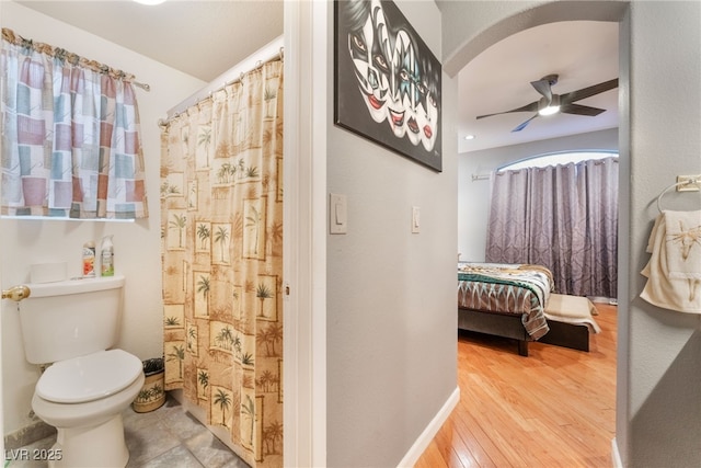 ensuite bathroom with connected bathroom, curtained shower, toilet, wood finished floors, and a ceiling fan