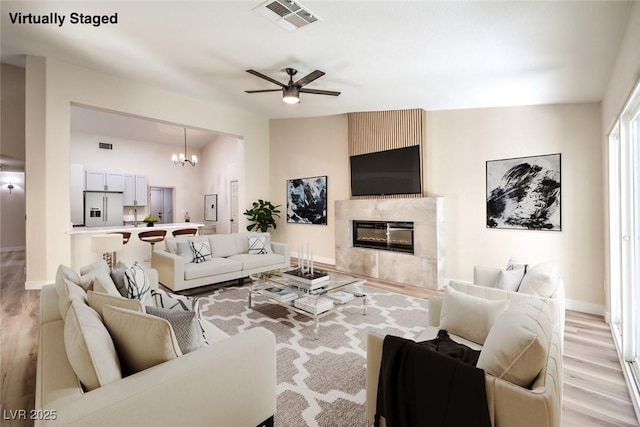 living room with visible vents, baseboards, a high end fireplace, light wood-style floors, and ceiling fan with notable chandelier