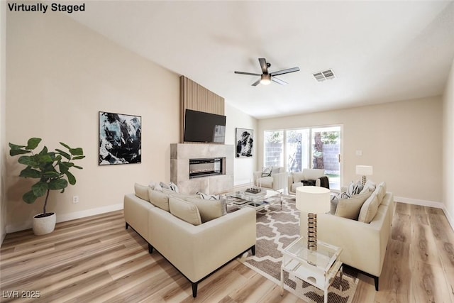 living room with vaulted ceiling, light wood-style flooring, visible vents, and a large fireplace