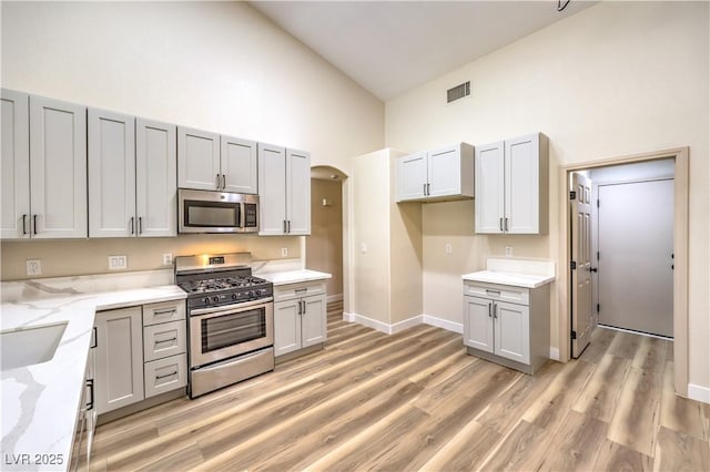 kitchen with visible vents, light stone countertops, high vaulted ceiling, arched walkways, and stainless steel appliances