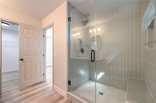 bathroom with a shower stall, wood finished floors, baseboards, and visible vents