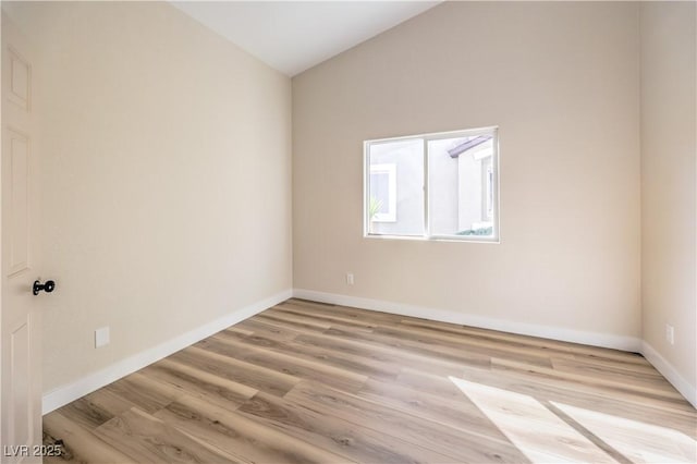 empty room with light wood-type flooring, baseboards, and vaulted ceiling