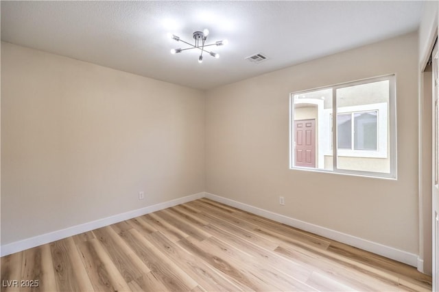 empty room with light wood finished floors, visible vents, and baseboards