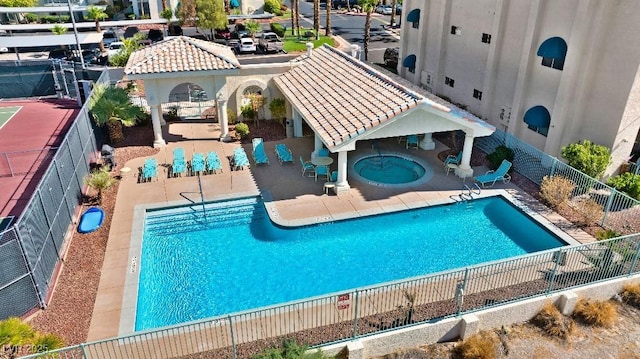 pool with a patio, a community hot tub, and fence