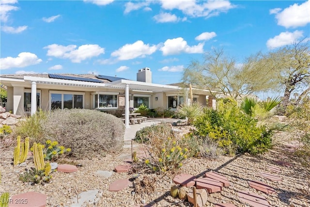 rear view of property with stucco siding, roof mounted solar panels, and a chimney