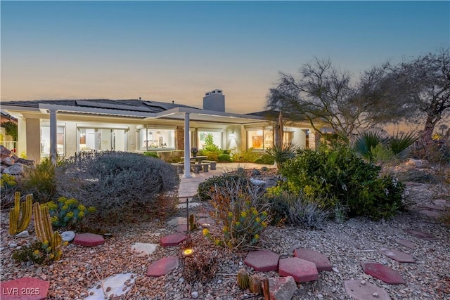 back of property at dusk with solar panels, a patio, stucco siding, and a chimney