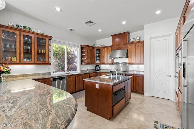 kitchen with dishwasher, visible vents, wall chimney range hood, dark stone counters, and a kitchen island with sink