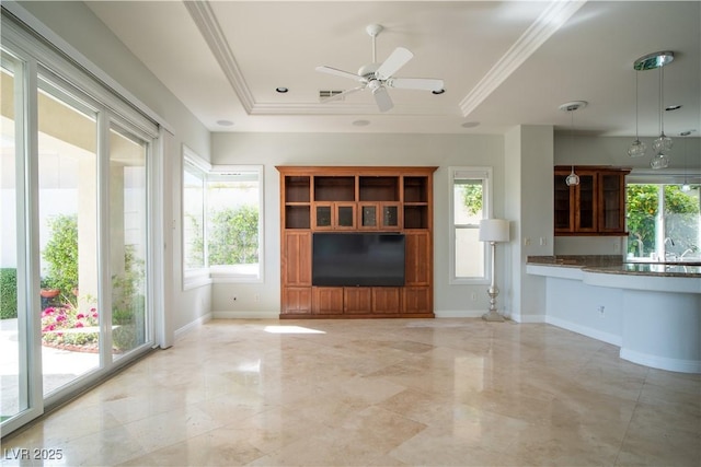 unfurnished living room featuring a tray ceiling, a healthy amount of sunlight, and baseboards