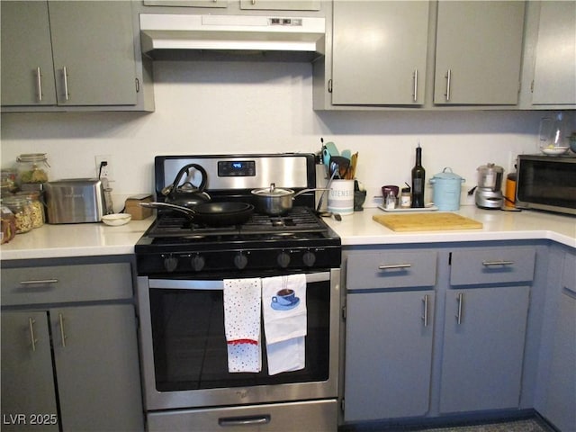 kitchen featuring under cabinet range hood, gas range, gray cabinetry, and light countertops