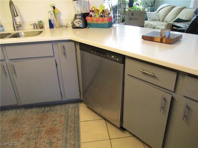 kitchen with gray cabinetry, dishwasher, light countertops, light tile patterned flooring, and a sink