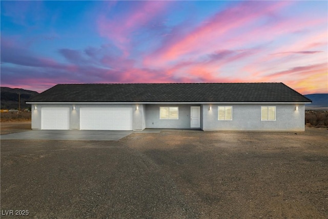 ranch-style home with aphalt driveway, an attached garage, and stucco siding