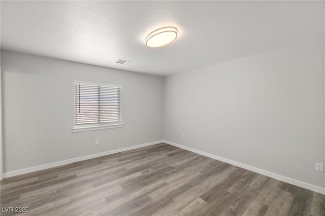 spare room featuring a textured ceiling, wood finished floors, visible vents, and baseboards