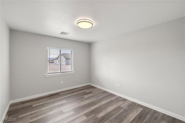 spare room featuring a textured ceiling, dark wood-style floors, visible vents, and baseboards