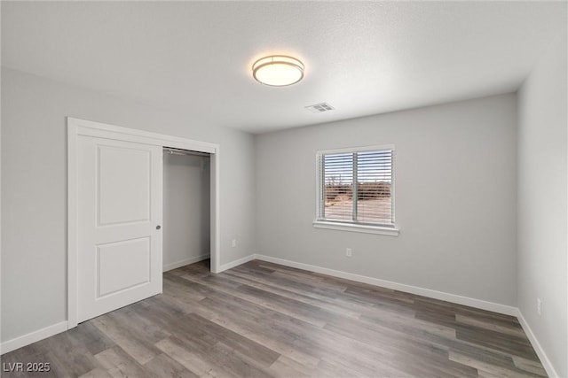 unfurnished bedroom with a closet, visible vents, baseboards, and wood finished floors