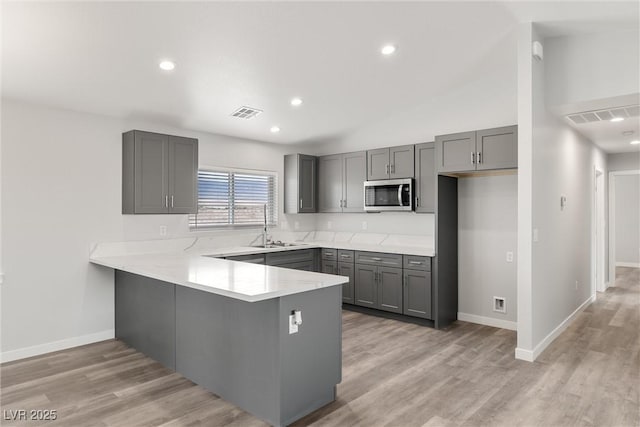 kitchen with stainless steel microwave, visible vents, gray cabinetry, and a peninsula