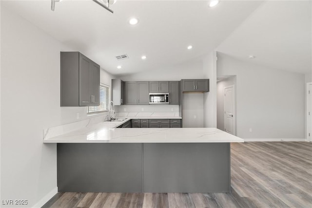 kitchen with light stone counters, visible vents, a peninsula, gray cabinetry, and stainless steel microwave