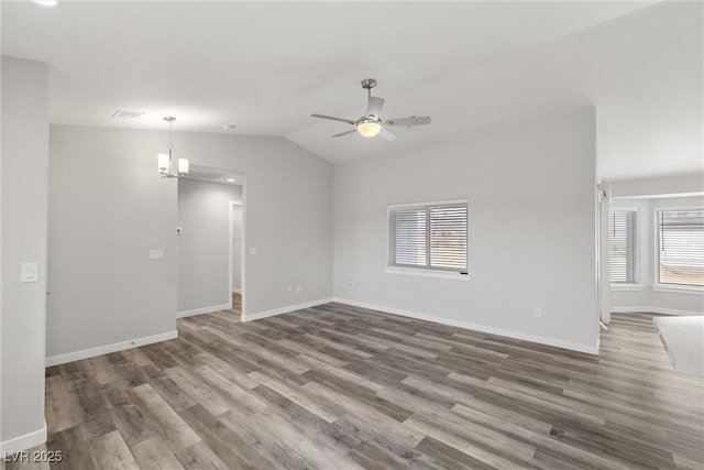 unfurnished living room with ceiling fan with notable chandelier, vaulted ceiling, wood finished floors, and baseboards