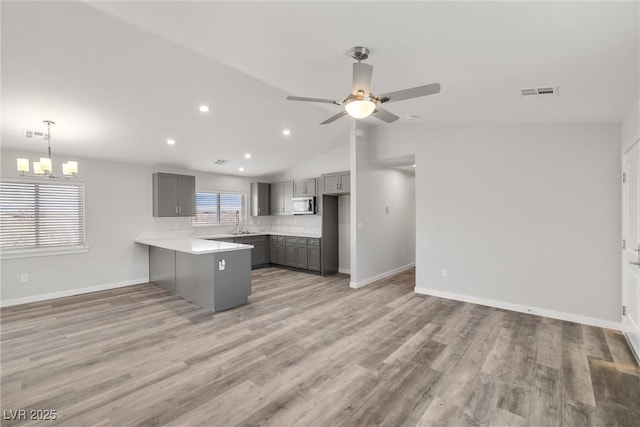 kitchen with stainless steel microwave, gray cabinetry, light wood-type flooring, and a peninsula