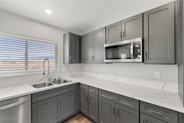 kitchen featuring a sink, light stone countertops, gray cabinets, and stainless steel appliances