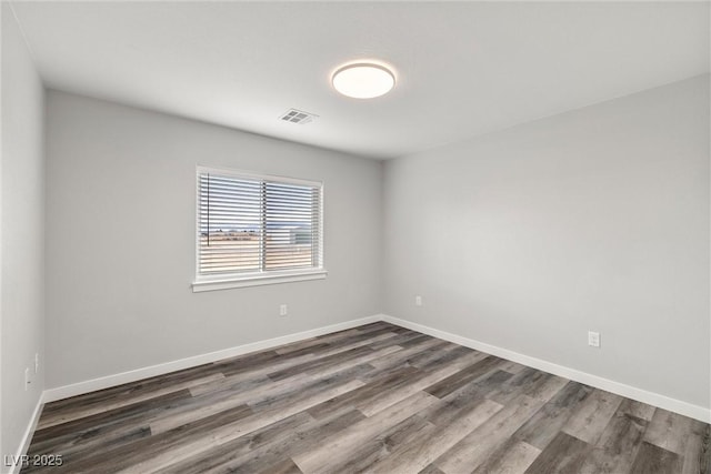 empty room with visible vents, dark wood-type flooring, and baseboards