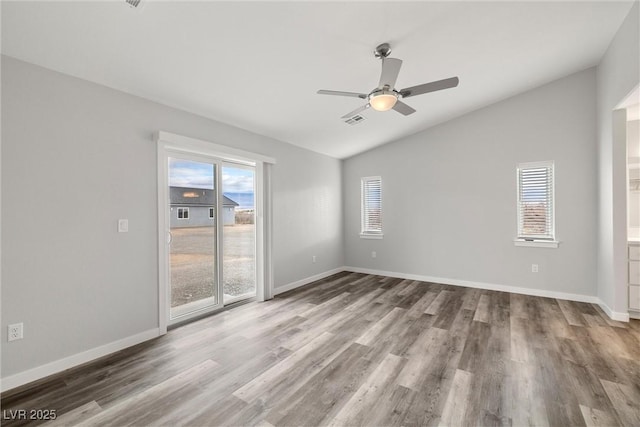 spare room with wood finished floors, visible vents, baseboards, ceiling fan, and vaulted ceiling