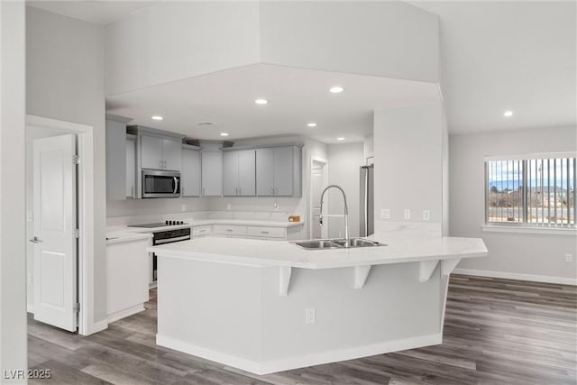 kitchen featuring a sink, stainless steel microwave, a peninsula, and gray cabinetry