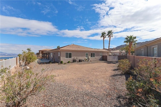 rear view of property featuring stucco siding, central AC unit, a fenced backyard, and a gate