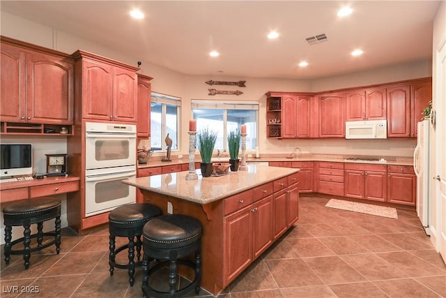 kitchen featuring open shelves, a kitchen island, white appliances, a breakfast bar area, and light stone countertops