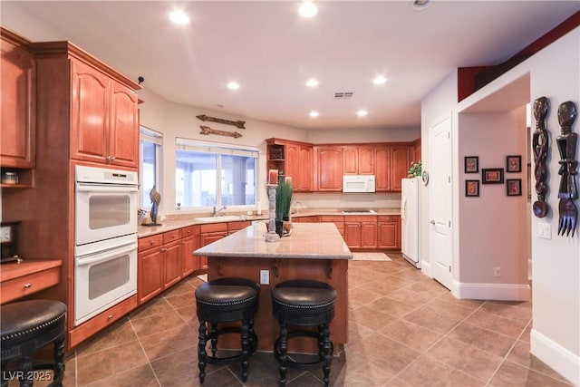 kitchen with visible vents, a center island, recessed lighting, white appliances, and a sink