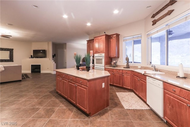 kitchen with a kitchen island, light countertops, a fireplace, white appliances, and a sink