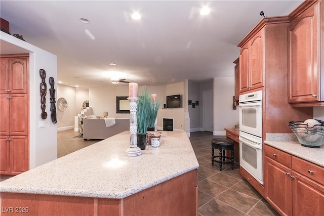 kitchen with a fireplace, white double oven, dark tile patterned floors, open floor plan, and a center island