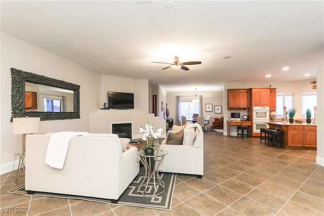 living room featuring baseboards, ceiling fan, light tile patterned floors, recessed lighting, and a glass covered fireplace